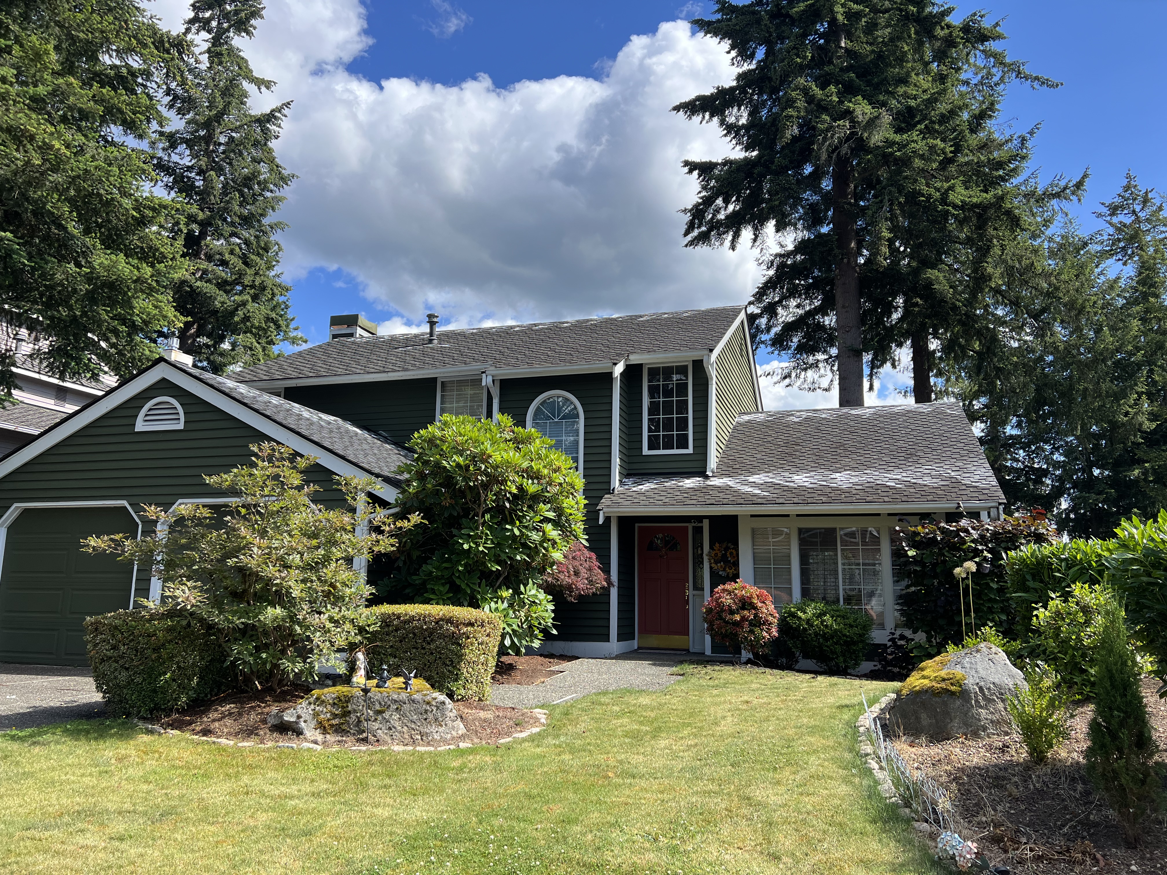The picture shows a typical two-story American house with a flowering garden, the roof of which is sprinkled with an anti-moss product. The photo shows an exterior roof cleaning with moss removal and moss control treatment by Beckman LLC The picture shows a typical two-story American house with a flowering garden, the roof of which is sprinkled with an anti-moss product. The photo shows an exterior roof cleaning with moss removal and moss control treatment by Beckman LLC